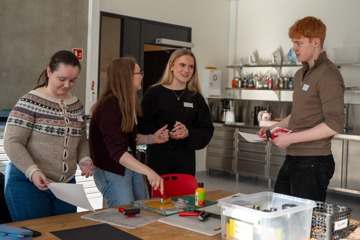 FIre elever smiler og holder papir og maling